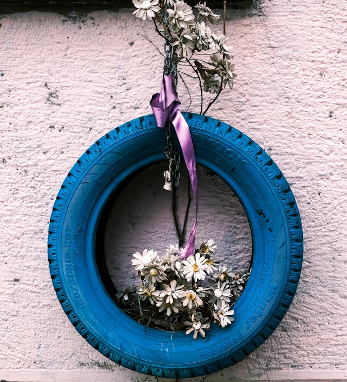 heros-img A blue tire repurposed as a decorative wall piece with daisies and a purple ribbon.