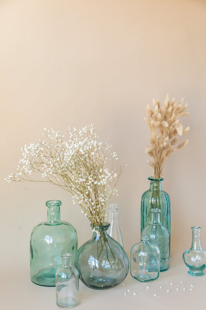 about-us Minimalist arrangement of recycled glass vases with dried flowers on a neutral background.